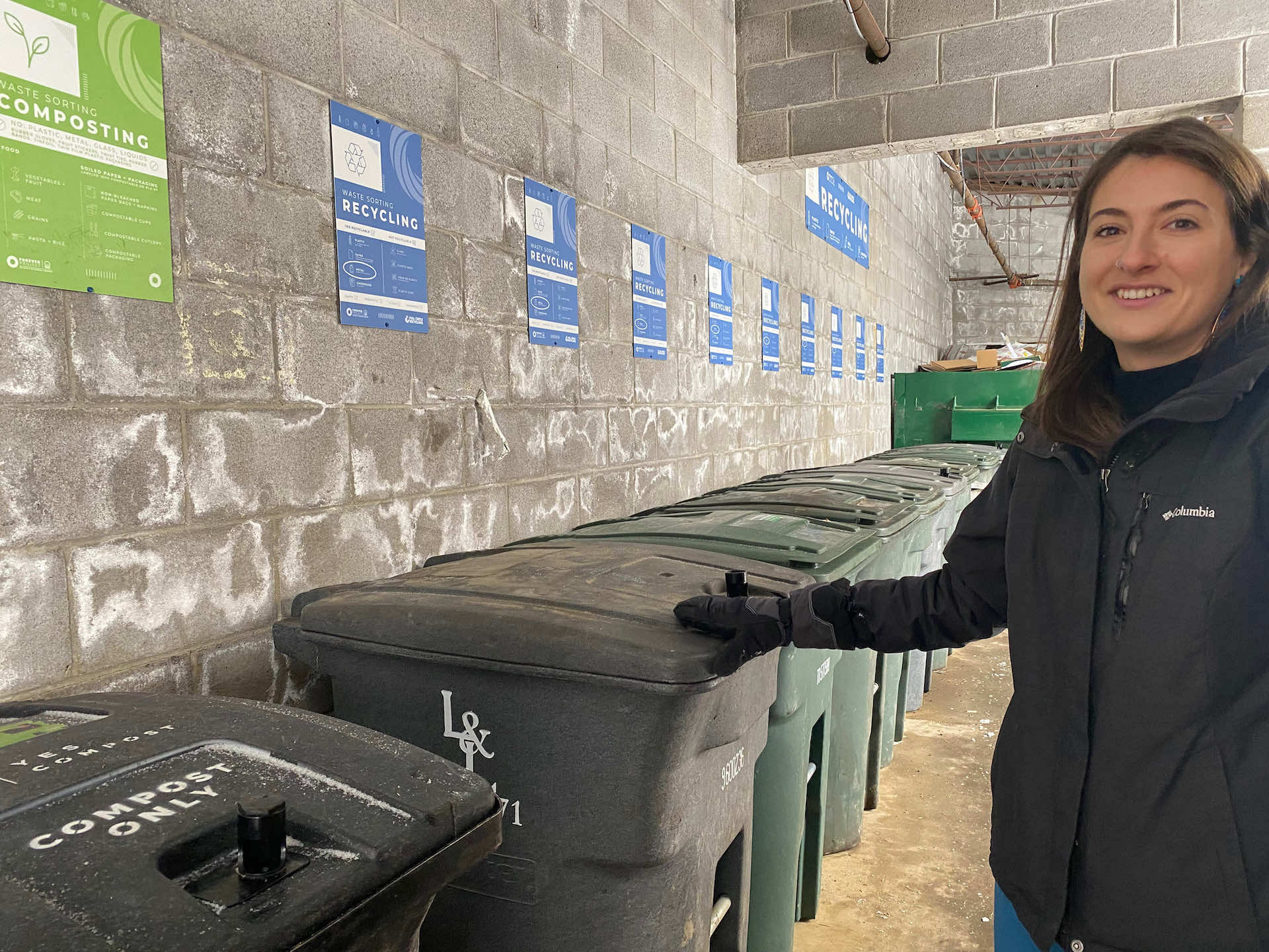 Amy stands near recycling bins
